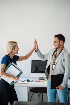 Two colleagues share a high-five in a modern office setting, showcasing teamwork and success.